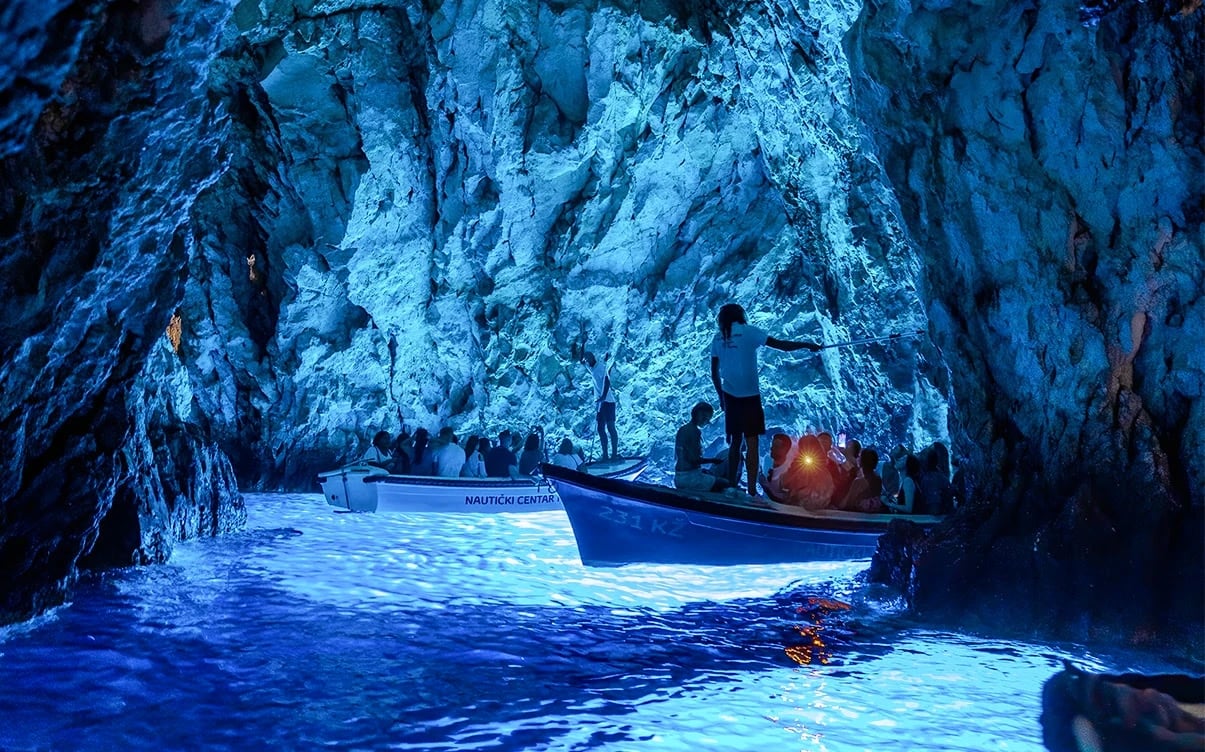 Small boats entering the Blue Cave on Biševo Island near Vis, Croatia, where sunlight creates a magical glowing blue light inside the cave.
