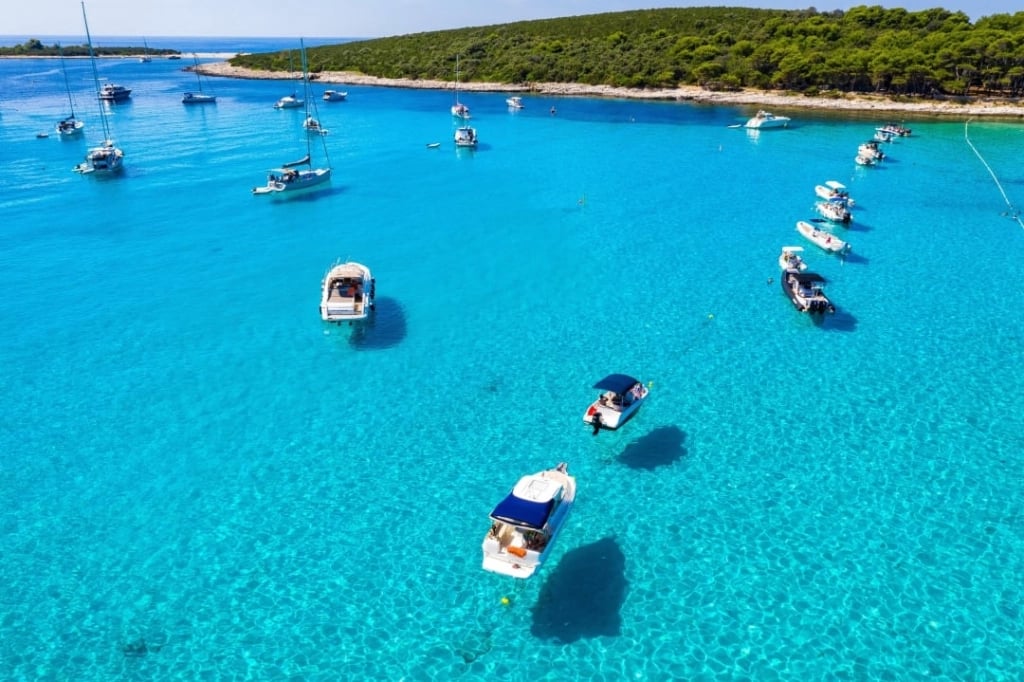 Drone view of the famous Blue Lagoon in Croatia with yachts and boats anchored in shallow turquoise water near Drvenik Islands.