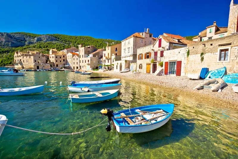 Traditional fishing boats in Komiža village on Vis Island, Croatia, with historic stone houses and crystal-clear Adriatic Sea – iconic stop on Dalmatian sailing routes.