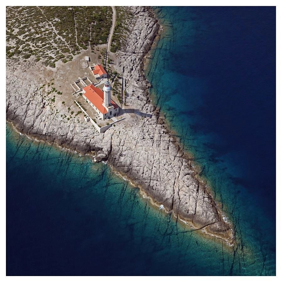Drone view of StonÄŤica Lighthouse on the eastern coast of Vis Island in Croatia, surrounded by turquoise Adriatic waters and rocky coastline.